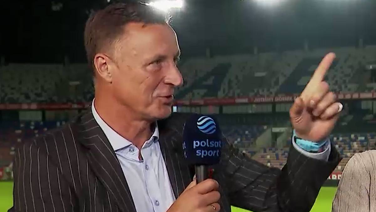 Mężczyzna w garniturze trzyma mikrofon Polsat Sport i wskazuje palcem w górę.