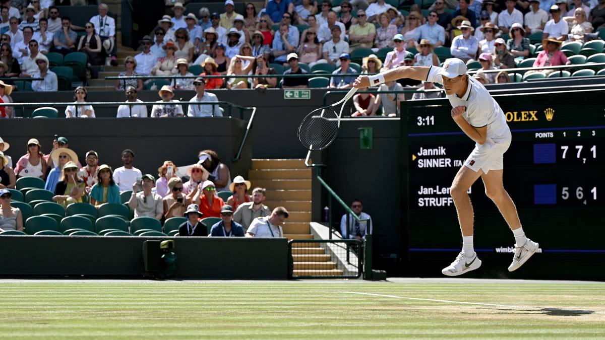 Zawodnik tenisa w akcji na korcie Wimbledonu, z publicznością na trybunach w tle.