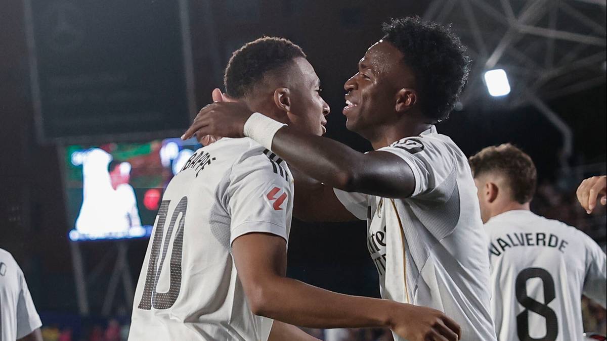 Dwóch piłkarzy w białych strojach świętuje razem, jeden z nich obejmuje drugiego za szyję.