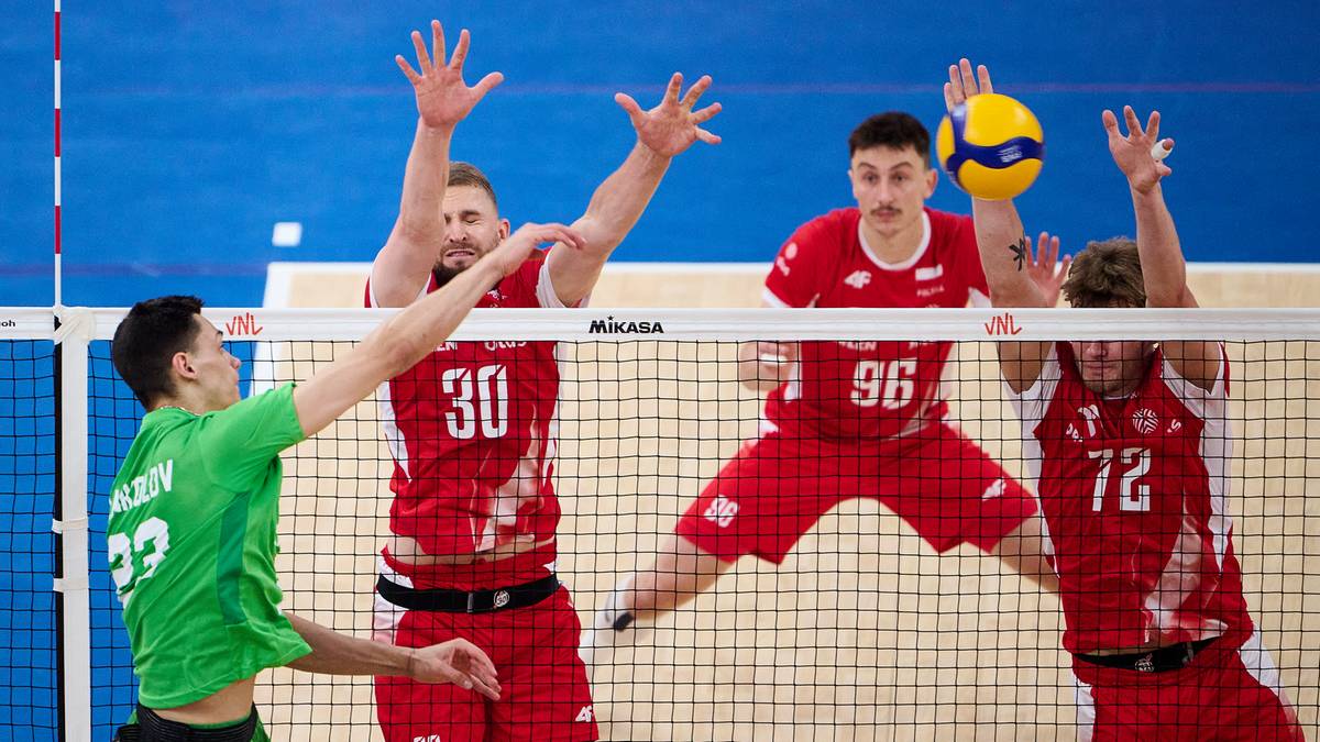 Sześciu mężczyzn grających w siatkówkę na boisku. Dwóch zawodników w czerwonych koszulkach próbuje zablokować piłkę nad siatką, jeden z nich wyskakuje do ataku. Dwóch innych zawodników w czerwonych koszulkach znajduje się za siatką, jeden z nich wykonuje zagranie. Zawodnik w zielonej koszulce próbuje zagrać piłkę przed siatką.