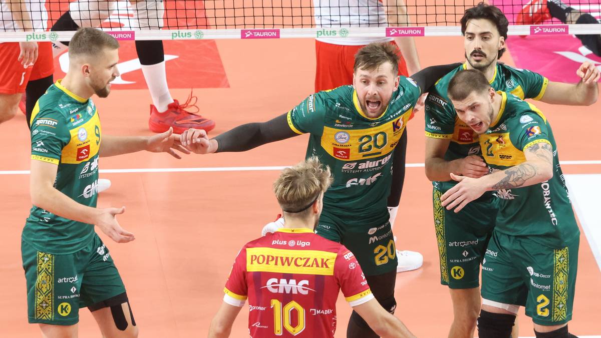 Siatkarze w zielonych strojach świętują zwycięstwo, jeden z nich unosi rękę w geście triumfu.