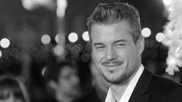 Portret czarno-biały aktora Erica Dane'a uśmiechającego się w stronę obiektywu, ubranego w białą koszulę i czarny garnitur.