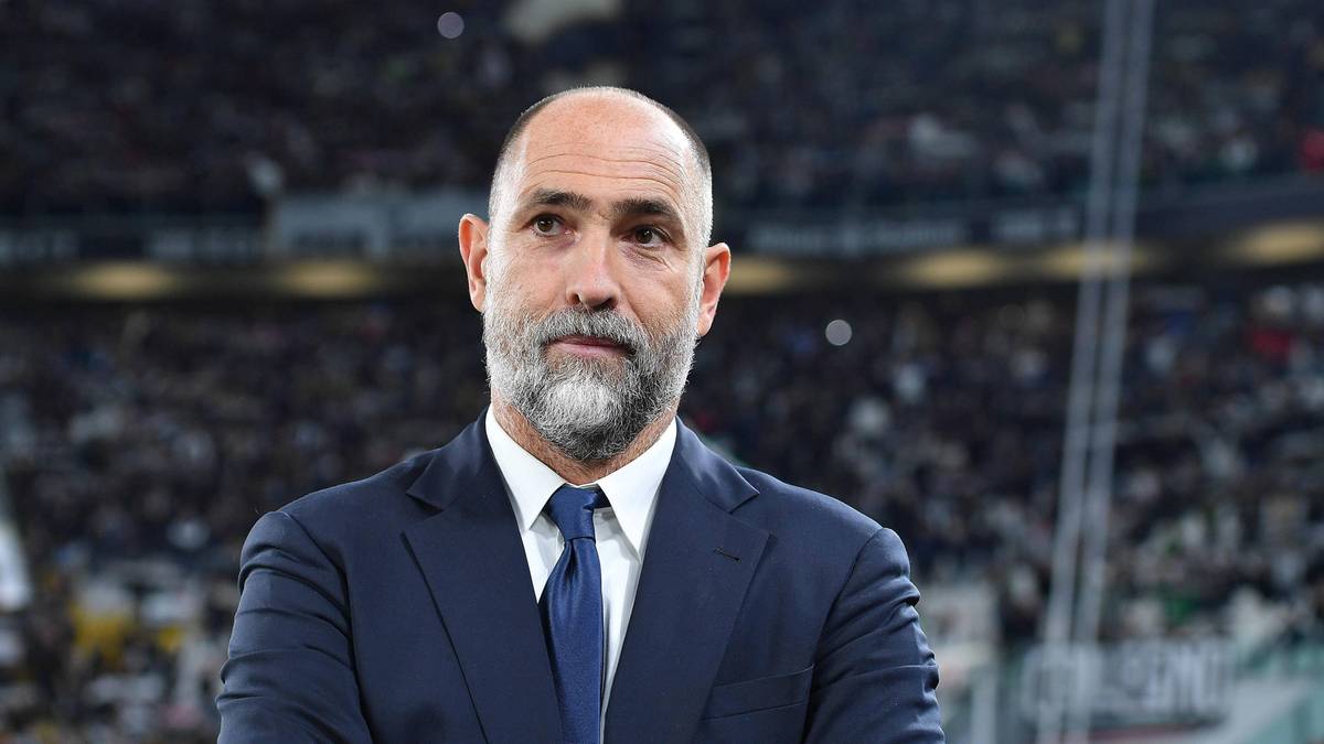 Portret mężczyzny w garniturze na tle stadionu piłkarskiego.