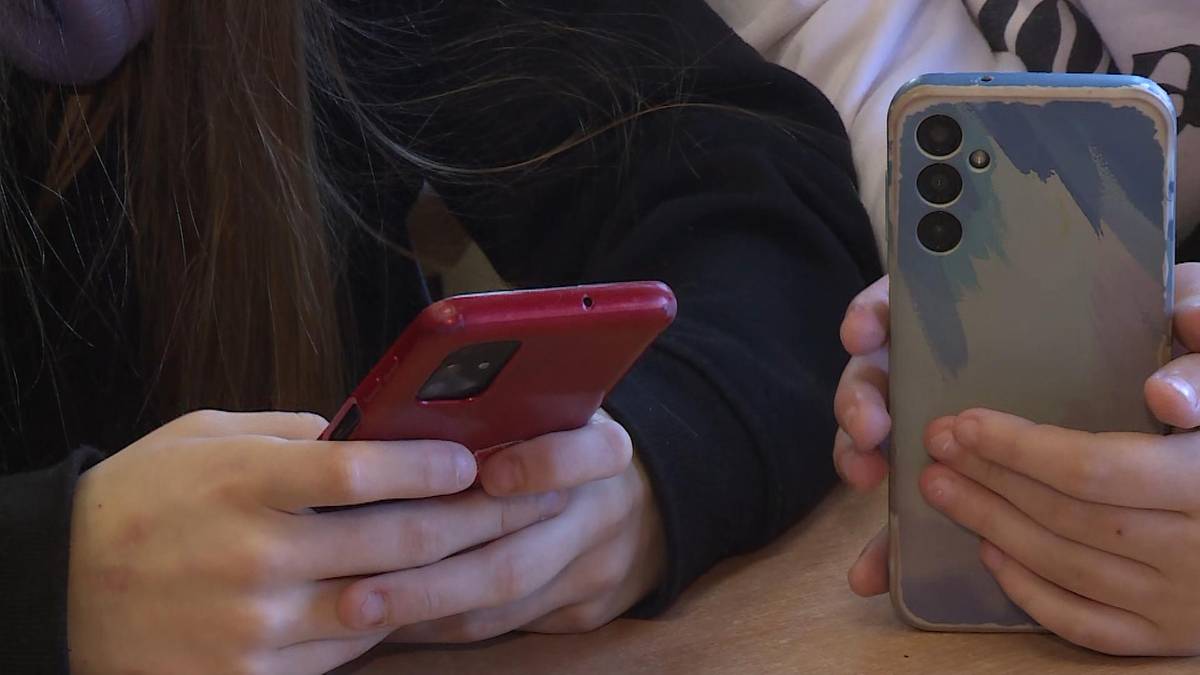 Dłonie dw&oacute;ch os&oacute;b trzymające smartfony. Jedna osoba trzyma czerwony telefon, druga srebrny z niebieskimi elementami.