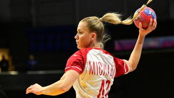 Zawodniczka piłki ręcznej w białej koszulce z czerwonymi detalami, wykonująca rzut.