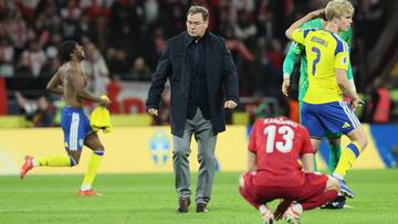 Trener reprezentacji Polski Jan Urban na boisku piłkarskim, otoczony przez zawodnik&oacute;w w barwach narodowych podczas meczu.