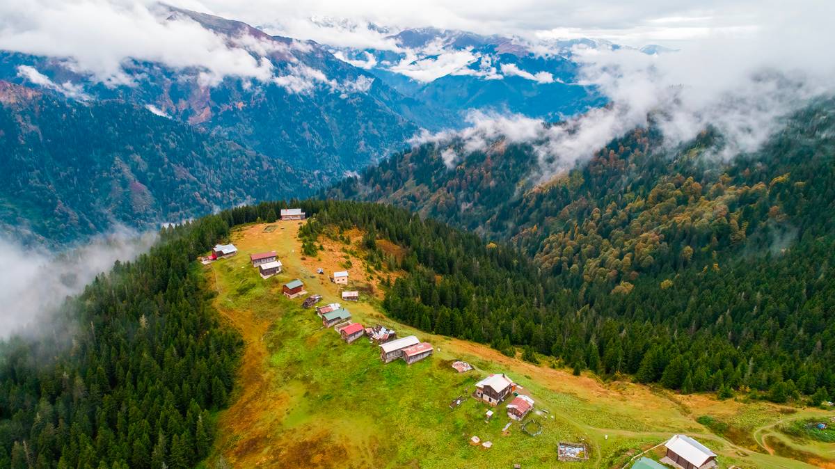 Górzysty krajobraz z lasami, mgłą i niewielką osadą na zboczu.