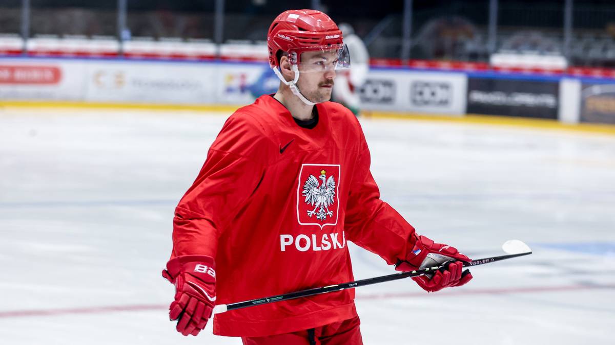 Hokeista w czerwonym stroju reprezentacji Polski trzyma kij hokejowy.