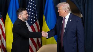 Wołodymyr Zełenski i Donald Trump ściskają sobie dłonie na tle flag Ukrainy i USA.