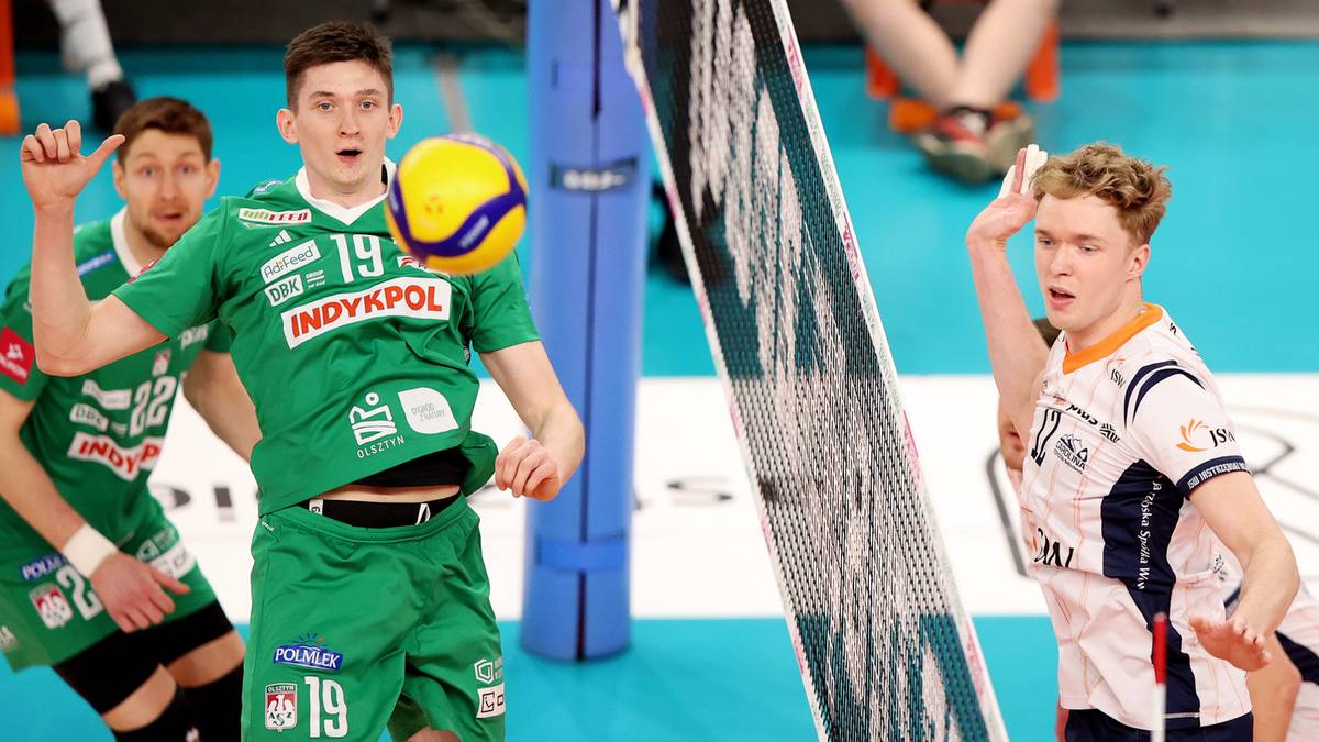 Dw&oacute;ch siatkarzy podczas meczu, jeden w zielonej koszulce z numerem 19 wykonuje zagrywkę, drugi w biało-niebieskiej koszulce.