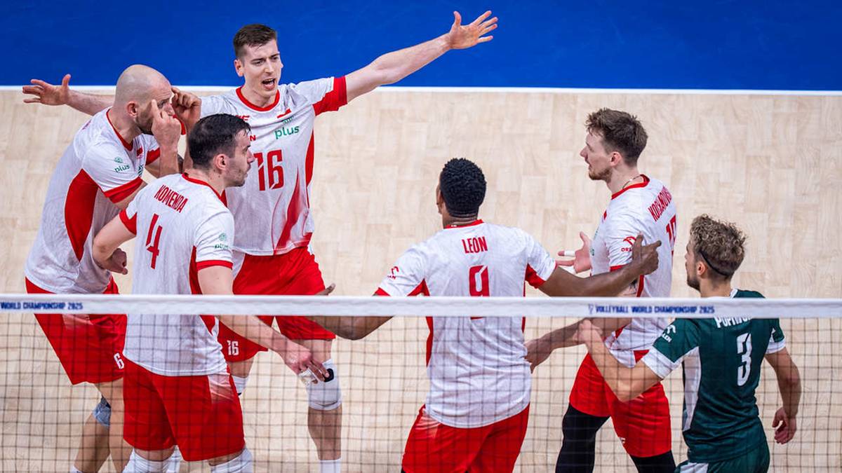 Sześciu siatkarzy w białych strojach z czerwonymi elementami, stojących na boisku, rozmawiających między sobą podczas przerwy w meczu.