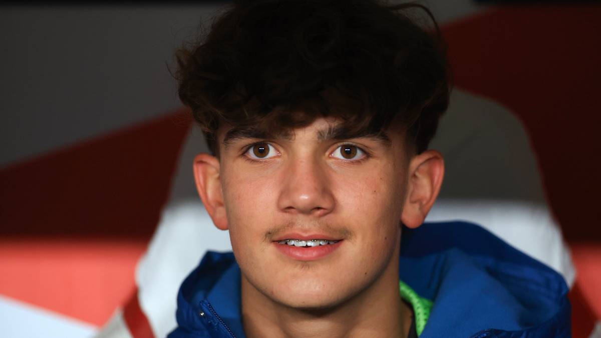 Młody mężczyzna o ciemnych kręconych włosach, patrzący w obiektyw, ubrany w niebieską kurtkę.