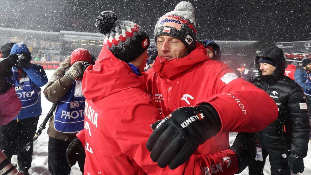 Dw&oacute;ch skoczk&oacute;w narciarskich w czerwonych kurtkach i czapkach zimowych przytulających się podczas opad&oacute;w śniegu.