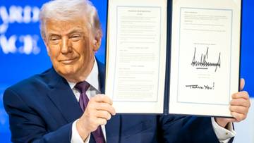 Donald Trump trzyma otwarty dokument z podpisami, prezentując go.