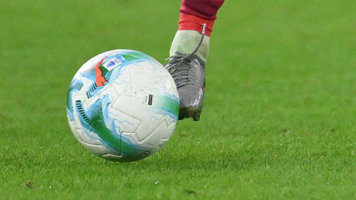 Piłkarz w czerwonej skarpecie i szarej stopce uderza piłkę nożną.