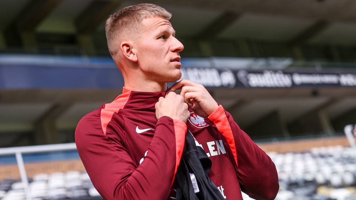 Młody piłkarz z blond włosami w koszulce sportowej zapatrzony w dal.