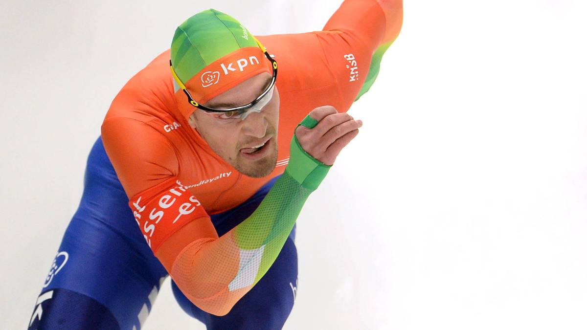 Holenderski panczenista w pomarańczowym stroju i zielonym czepku, pochylony podczas jazdy na łyżwach.