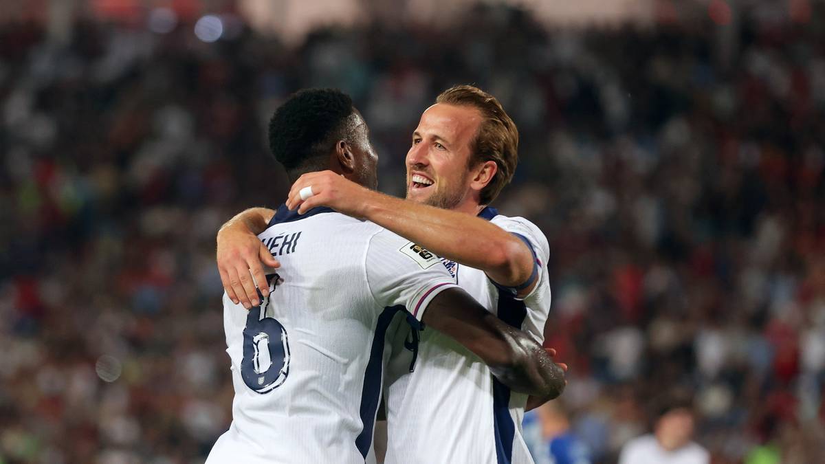 Dwóch piłkarzy w białych koszulkach reprezentacji Anglii świętuje gola, obejmując się. Jeden z nich, Harry Kane, z uśmiechem na twarzy obejmuje swojego kolegę z drużyny.