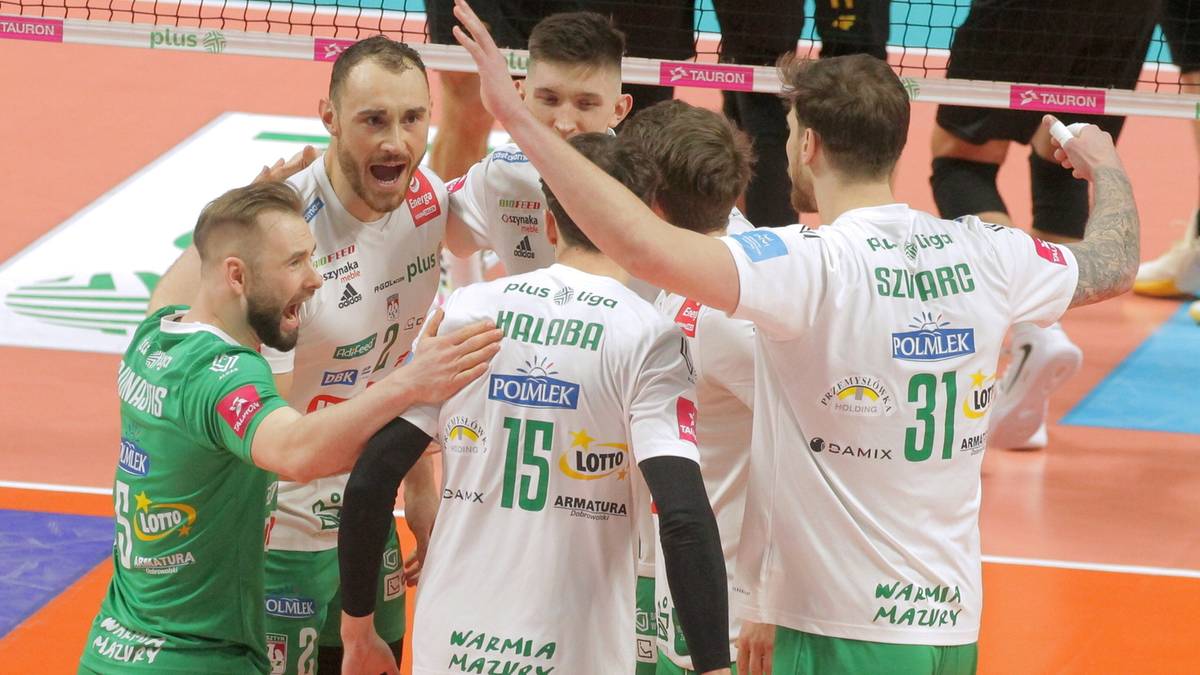 Grupa siatkarzy w białych strojach świętuje na boisku, podając sobie ręce i przytulając się.