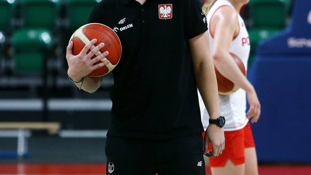 Trener w czarnej koszulce z herbem Polski trzyma piłkę do koszyk&oacute;wki.