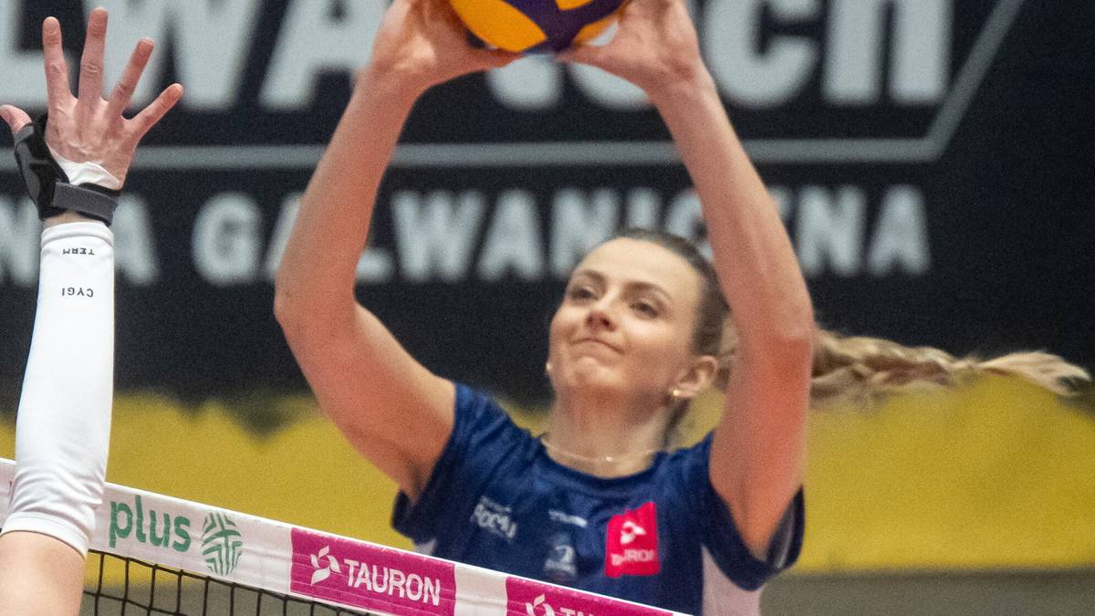 Siatkarka w niebieskim stroju z numerem 12 szykuje się do zbicia piłki, podczas gdy dwie zawodniczki w białych strojach z numerem 14 próbują ją zablokować.