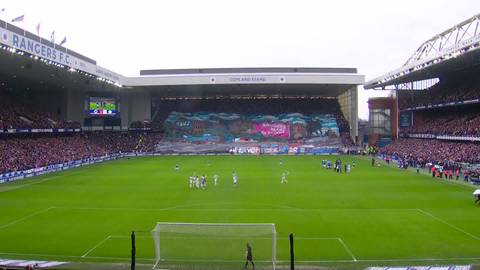 Piłkarze na murawie stadionu podczas meczu Rangers - Celtic, trybuny wypełnione kibicami.