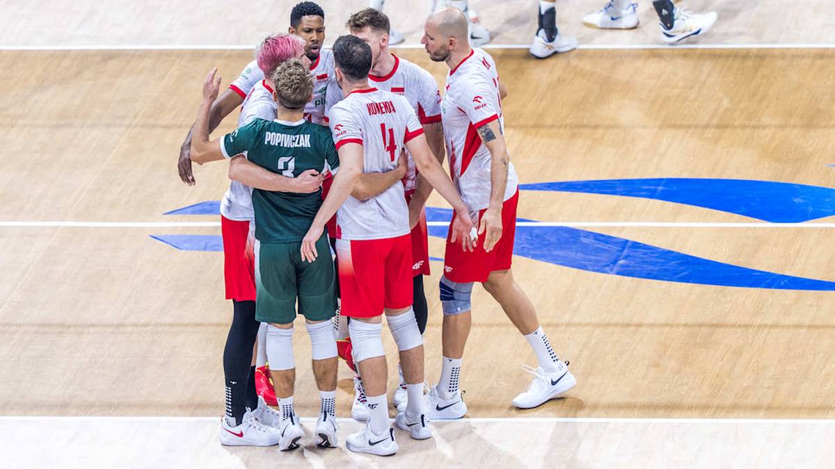 Drużyna siatkarzy w białych i zielonych strojach tworzy grupę na parkiecie hali sportowej.