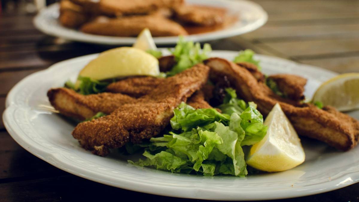 Talerz z panierowanymi kawałkami ryby podanymi z sałatką i ćwiartkami cytryny.