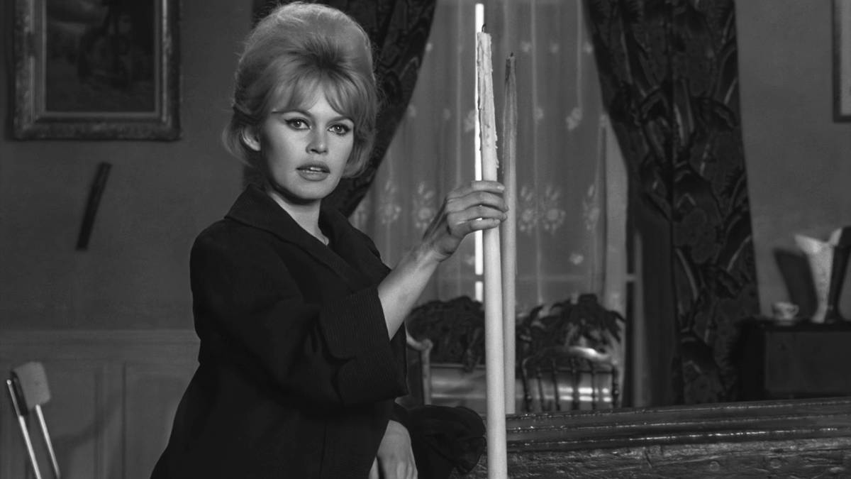 Brigitte Bardot w czarnej sukience i żakiecie, z charakterystyczną fryzurą, opiera się o kij bilardowy.