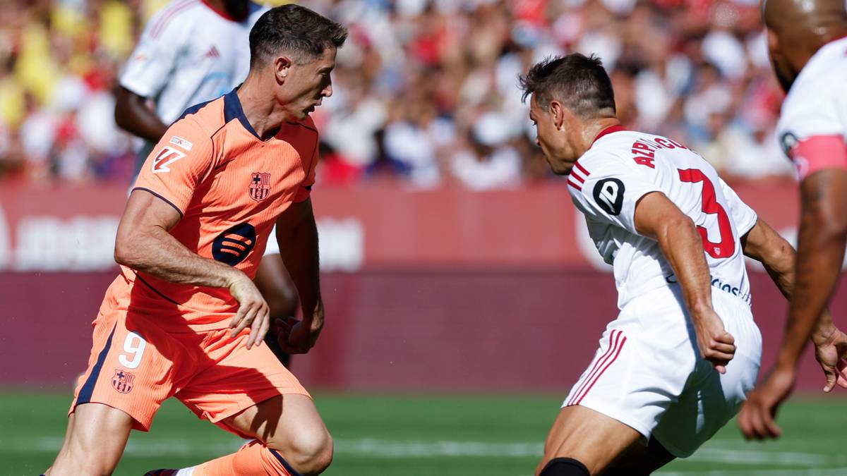 Piłkarze w akcji na boisku, jeden w pomarańczowej koszulce z numerem 9, drugi w białej z numerem 3.