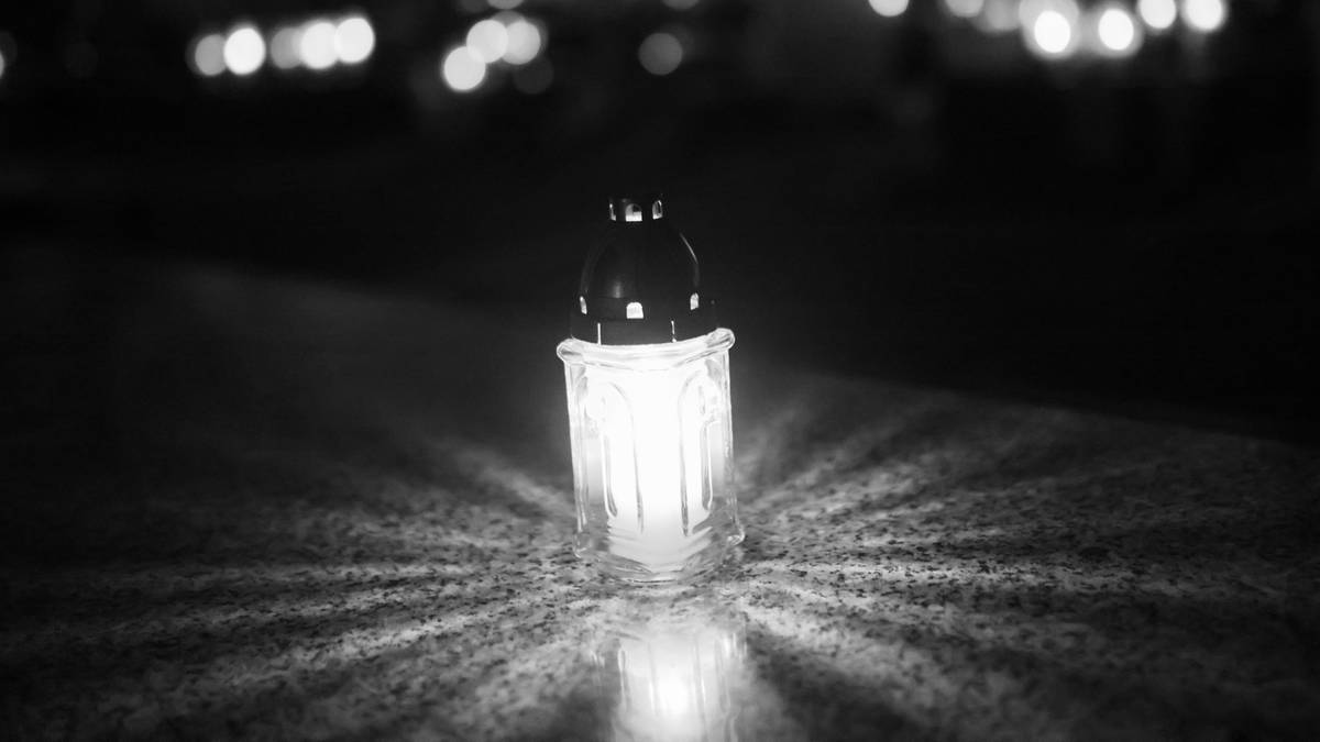 Znicz płonący w ciemności, z rozchodzącymi się promieniami światła. W tle widoczne są rozmyte światła.