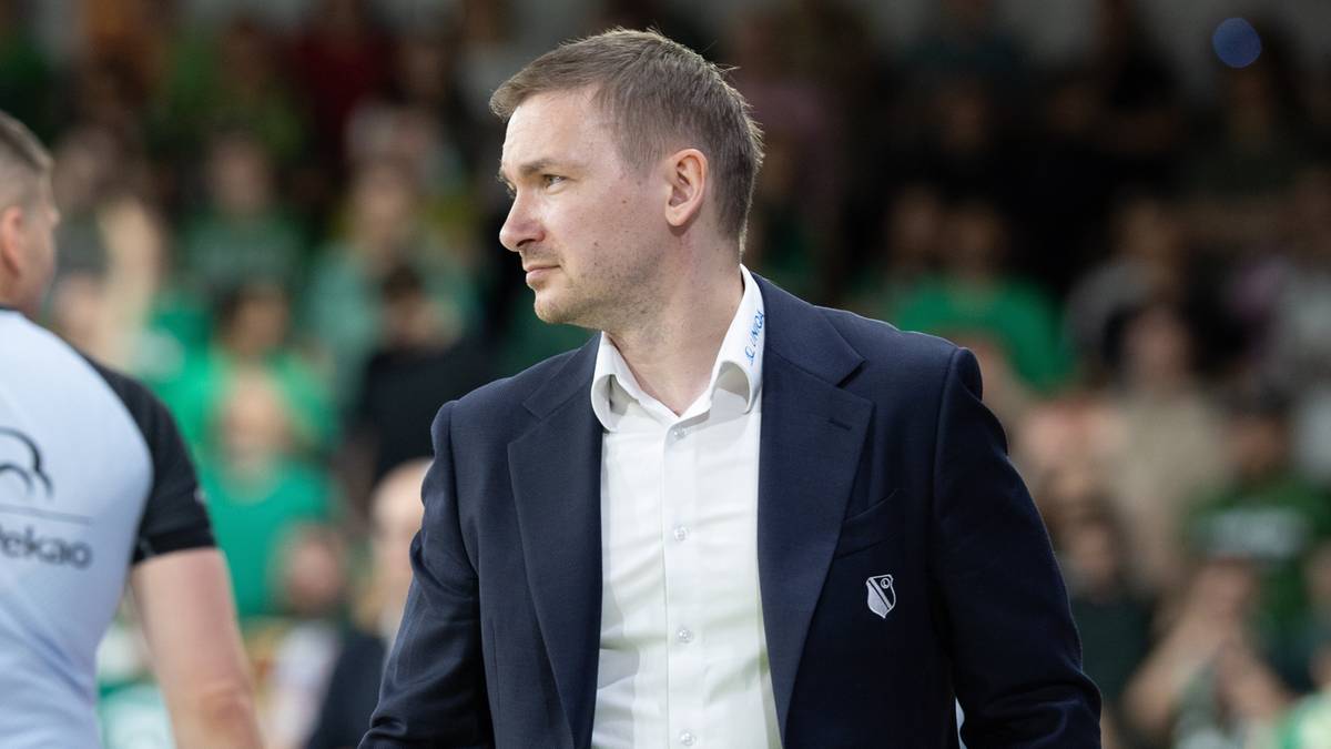 Dw&oacute;ch mężczyzn na tle kibic&oacute;w na hali sportowej, jeden w garniturze, drugi w stroju sportowym.