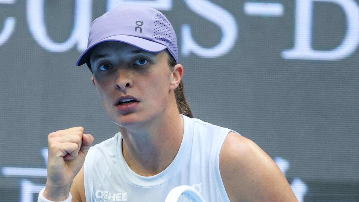 Iga Świątek unosi pięść w geście radości, trzymając rakietę tenisową.