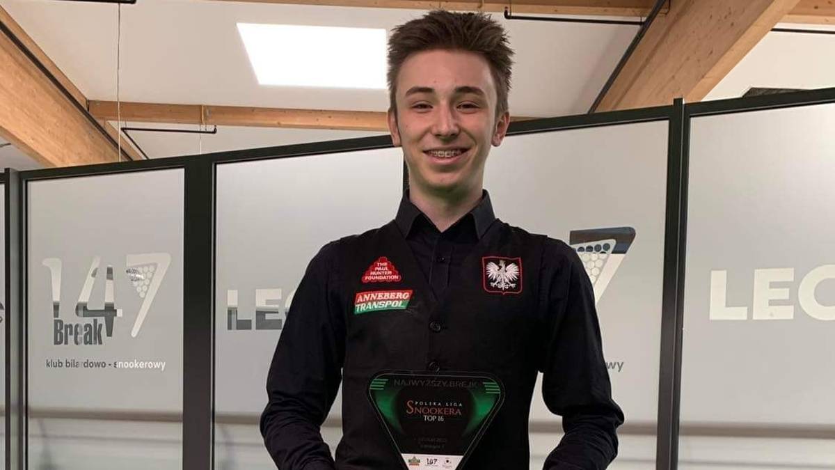 Młody mężczyzna w czarnej koszuli trzyma puchar snookerowy.