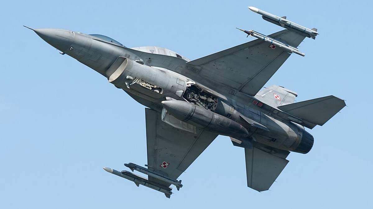 Myśliwiec F-16 w locie, uzbrojony, na tle błękitnego nieba.