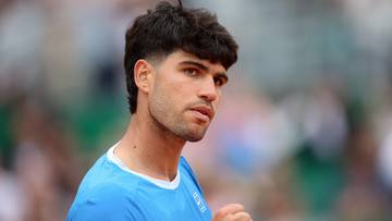 Carlos Alcaraz, hiszpański tenisista, w błękitnej koszulce, zapatrzony w bok z zaciśniętą pięścią.