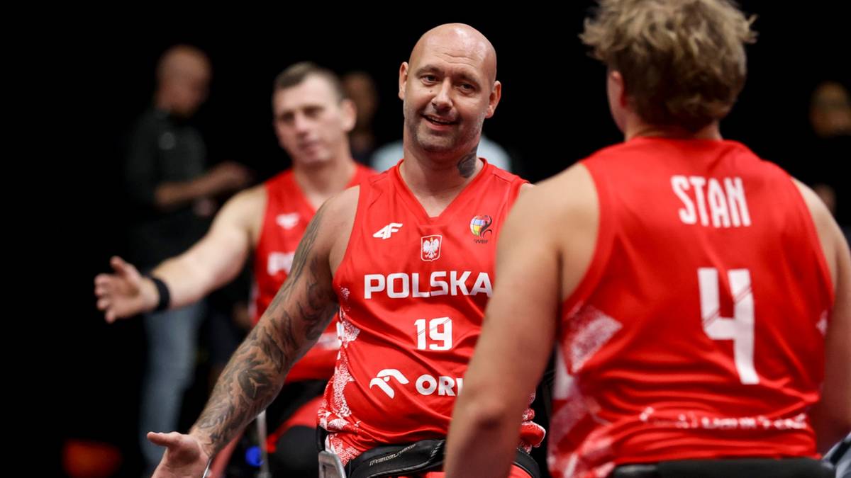 Trzech polskich koszykarzy w czerwonych koszulkach z orzełkiem na piersi, uśmiechających się. Jeden z nich, łysy, z tatuażem na szyi, ma na koszulce napis "POLSKA" i numer "19". Pozostali dwaj zawodnicy również noszą koszulki z biało-czerwonymi barwami narodowymi.