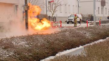 Płomienie wydobywające się ze słupa, strażak w pobliżu, biały pojazd.