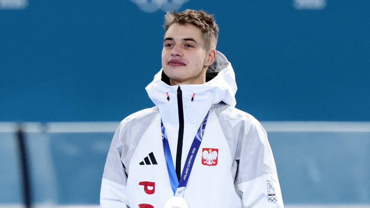 Polski łyżwiarz Semirunnij z medalem na szyi, ubrany w białą kurtkę sportową z biało-czerwonym godłem Polski.