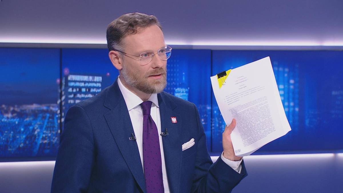 Mężczyzna w garniturze i krawacie trzyma dokument.