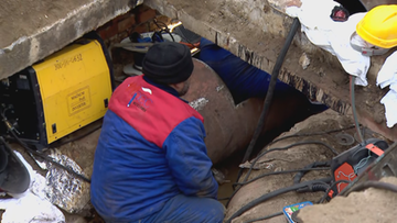 Pracownicy naprawiający dużą, podziemną rurę ciepłowniczą.