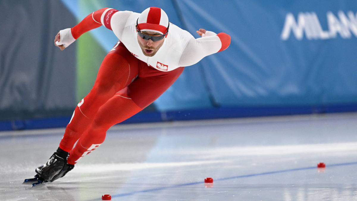 Polski łyżwiarz szybki w kombinezonie biało-czerwonym pędzi po lodowisku, pochylony do przodu.