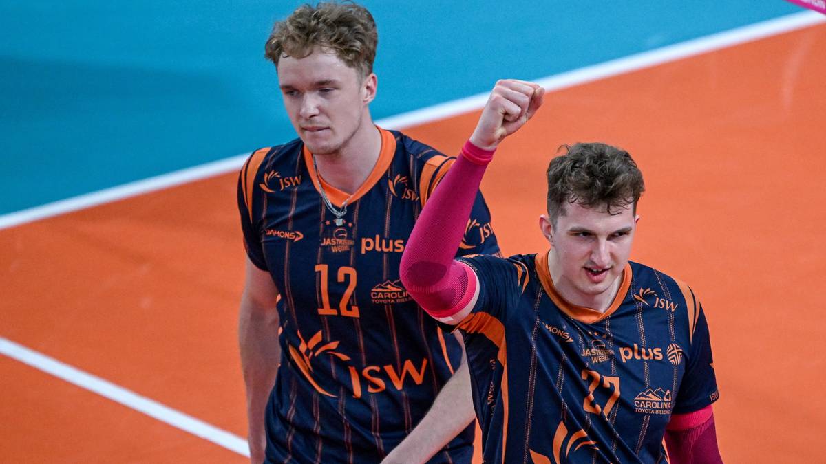 Dw&oacute;ch siatkarzy w strojach sportowych JSW Jastrzębski Węgiel z numerami 12 i 27 na koszulkach, stojących na boisku siatkarskim.