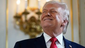 Donald Trump uśmiecha się, ubrany w garnitur i czerwoną muszkę.