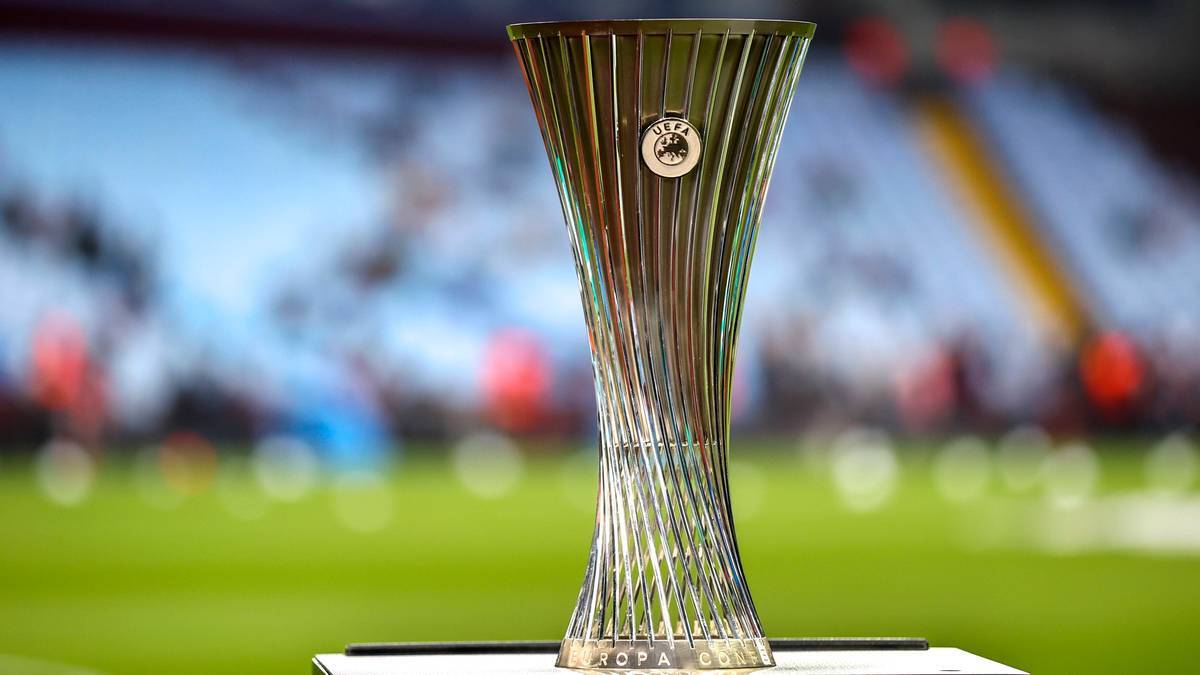 Kryształowe trofeum pucharu piłkarskiego na tle stadionu.