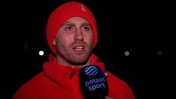 Zbliżenie na twarz Damiana Żurka w czerwonej czapce i bluzie, trzymającego mikrofon Polsat Sport.
