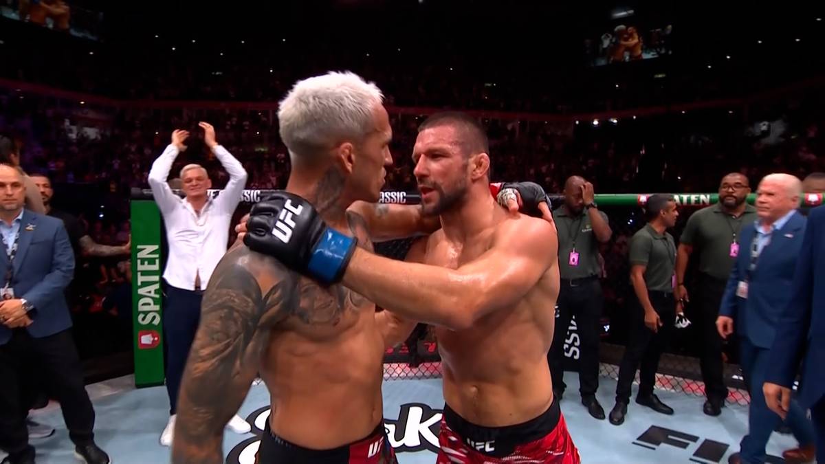 Dwóch zawodników MMA po walce obejmuje się, okazując wzajemny szacunek. Jeden z nich ma krótkie blond włosy, drugi ciemne.