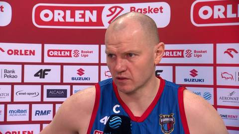 Damian Kulig, koszykarz w stroju sportowym, na tle ścianki sponsorskiej.