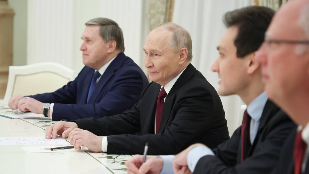 Prezydent Rosji Władimir Putin siedzi przy stole z innymi mężczyznami podczas spotkania.