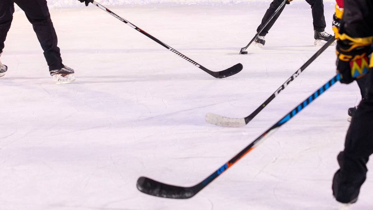 Hokeiści na lodowisku, widoczne kije hokejowe.